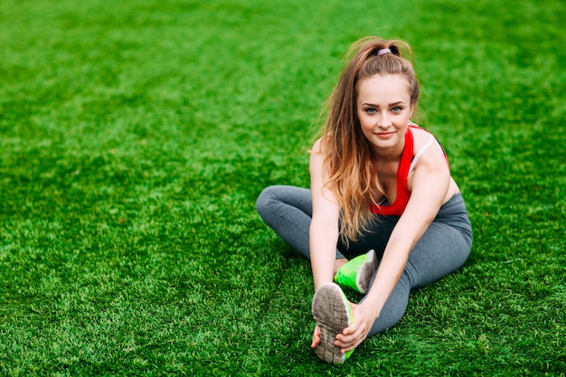 Mujer joven fitness sentada sobre la hierba verde.