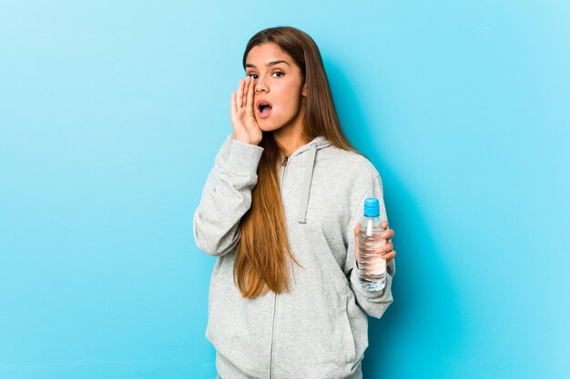 Mujer joven fitness sosteniendo una botella de agua gritando emocionado al frente.