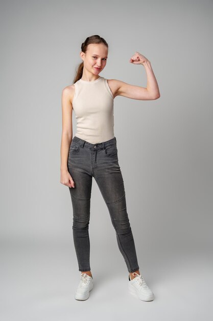 Mujer joven flexionando los músculos en una camiseta beige sobre un fondo gris