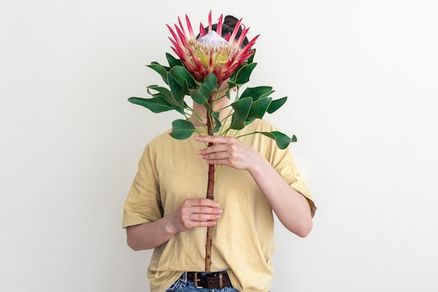 Una mujer joven con flor protea sobre un fondo blanco.