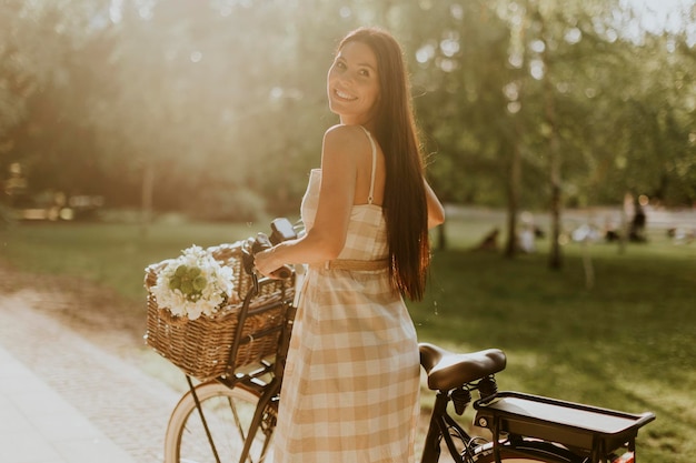 Mujer joven con flores en la cesta de la bicicleta eléctrica