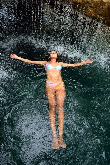 mujer joven, flotar, en, agua, en, piscina, con, cascada