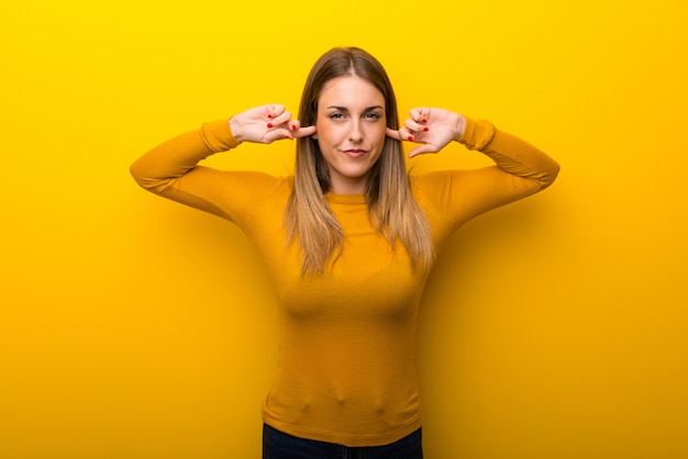 Foto mujer joven en el fondo amarillo que cubre ambos oídos con las manos