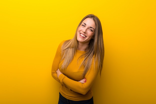 Mujer joven en el fondo amarillo que mantiene los brazos cruzados mientras que sonríe