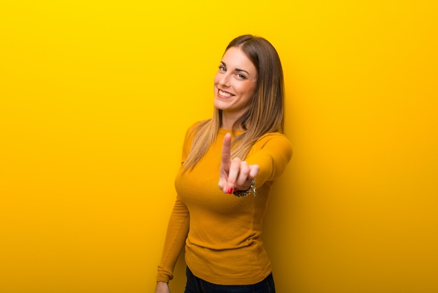 Foto mujer joven en el fondo amarillo que muestra y que levanta un dedo