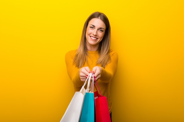 Foto mujer joven en el fondo amarillo que sostiene muchos bolsos de compras