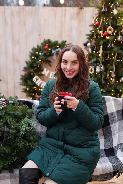 mujer joven, en, fondo, de, árbol de navidad, con, taza de café, al aire libre, patio trasero, decoración, año nuevo