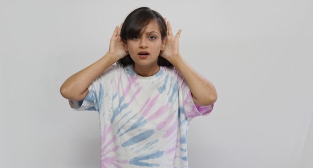 Mujer joven en un fondo gris aislado escuchando algo poniendo una mano en la oreja