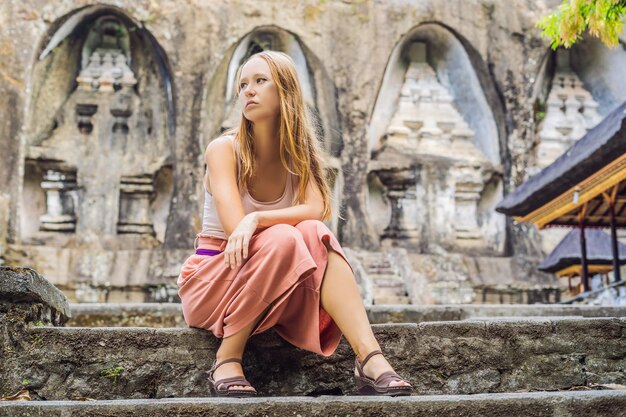 Mujer joven en el fondo de Gunung Kawi. Antiguo tallado en el templo de piedra con tumbas reales. Bali, Indonesia.