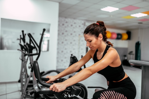 Mujer joven en forma haciendo ejercicio en bicicleta de gimnasio.