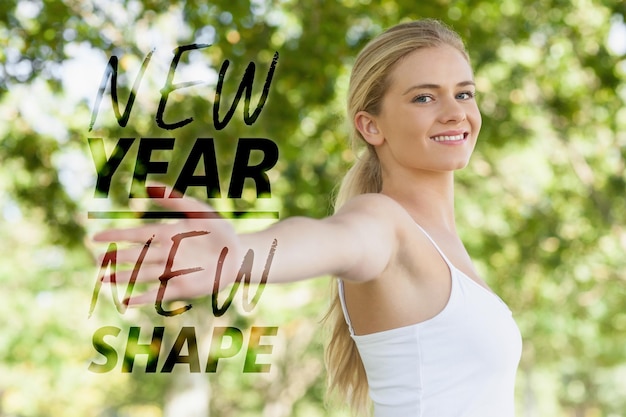 Mujer joven en forma haciendo yoga en un parque extendiendo sus brazos contra la nueva forma de año nuevo