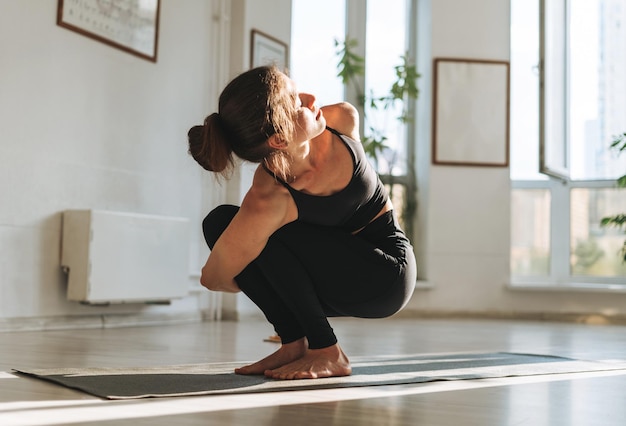 Mujer joven en forma practica yoga haciendo asana en estudio de yoga ligero con planta de casa verde