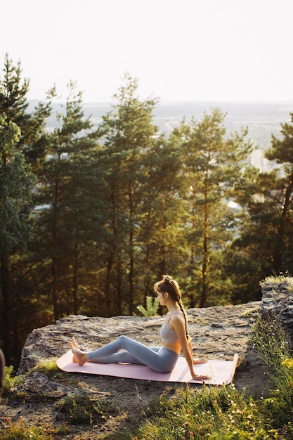 Foto mujer joven en forma practica yoga en las rocas contra el fondo del bosque de pinos