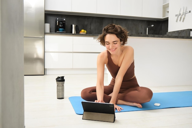 Mujer joven en forma y saludable instructora de yoga fitness chica en chándal se sienta en el piso con alfombra de goma