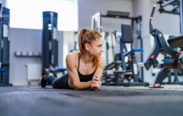 Mujer joven en forma tendida en el suelo y haciendo ejercicios estomacales en el club deportivo Mujer joven cansada relajándose después de un entrenamiento en un gimnasio con una mirada seria y pensativa a un lado