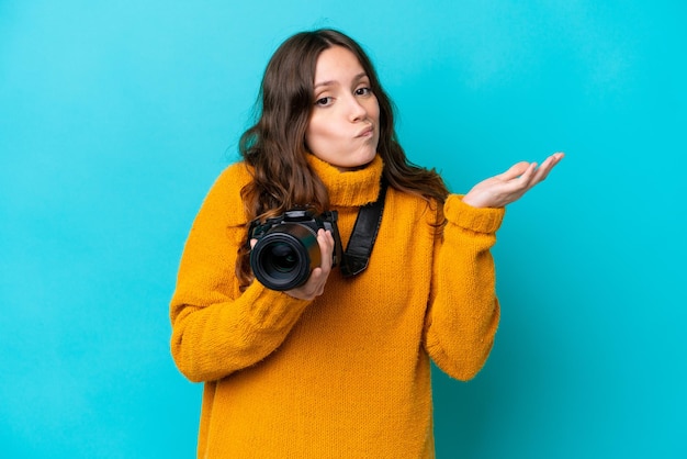 Mujer joven fotógrafa aislada de fondo azul que tiene dudas mientras levanta las manos