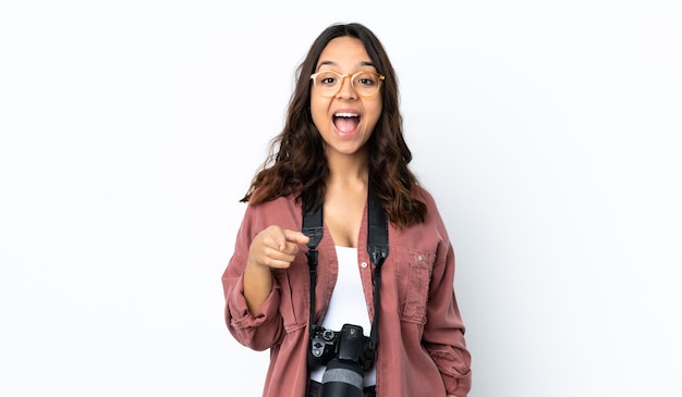 Mujer joven fotógrafo sobre fondo blanco aislado sorprendido y apuntando hacia el frente