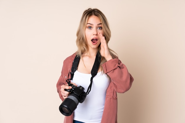 Mujer joven fotógrafo sobre pared aislada con sorpresa y expresión facial conmocionada