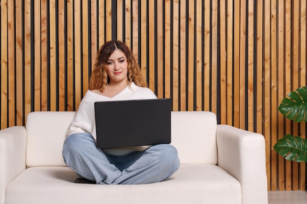 Mujer joven freelance está en casa en el sofá, usando una computadora portátil