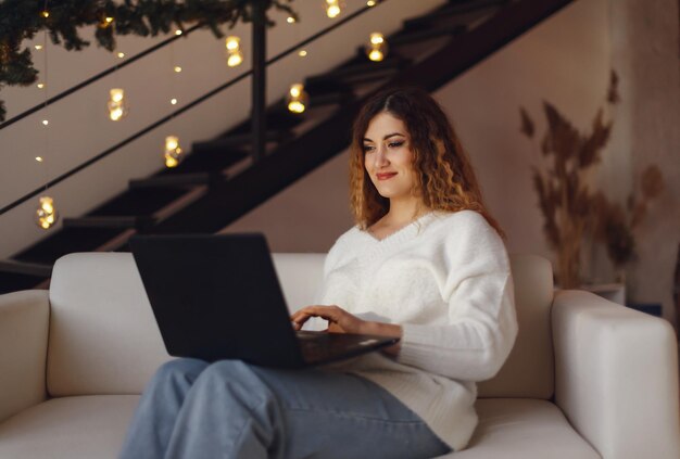 Mujer joven freelance está en casa en el sofá, usando una computadora portátil