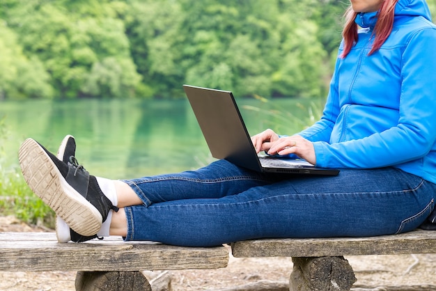 Foto mujer joven freelance trabajando con ordenador portátil con hermosa vista del bosque y el lago