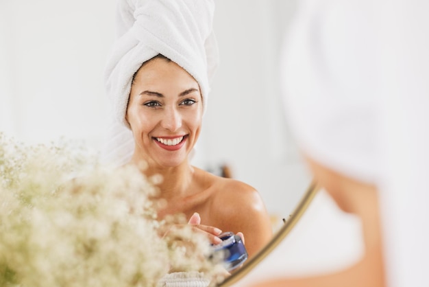 Mujer joven frente al espejo pasando por su rutina de belleza matutina en el baño de su casa.