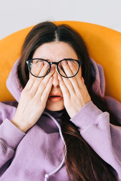 Mujer joven se frota los ojos después de usar gafas en la computadora portátil frontal. Concepto de fatiga o dolor ocular.