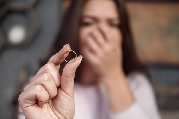 mujer joven frustrada que sostiene el anillo en la mano, llorando