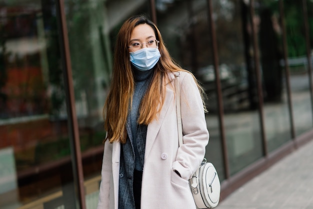 Mujer joven fsian con mascarilla está de pie en una calle doméstica. Concepto nuevo normal de viajeros después de la epidemia de covid-19