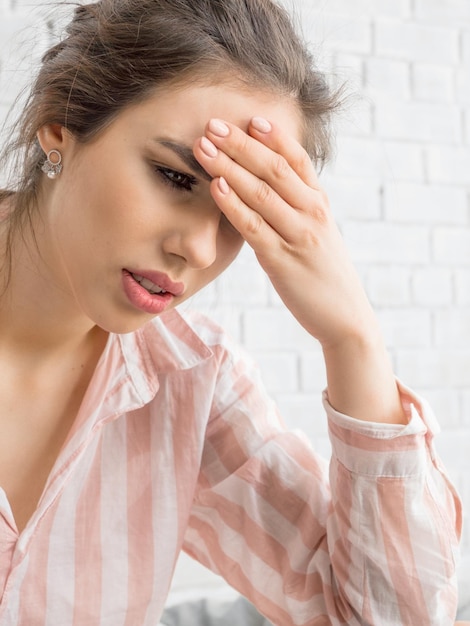 Mujer joven con fuerte dolor de cabeza, se sostiene la frente y trata de lidiar con el dolor