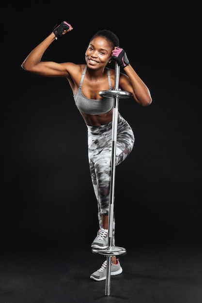 Mujer joven fuerte con hermoso cuerpo atlético haciendo ejercicios con barra aislada en una pared negra