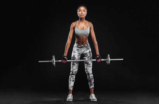 Mujer joven fuerte con hermoso cuerpo atlético haciendo ejercicios con barra aislada en una pared negra