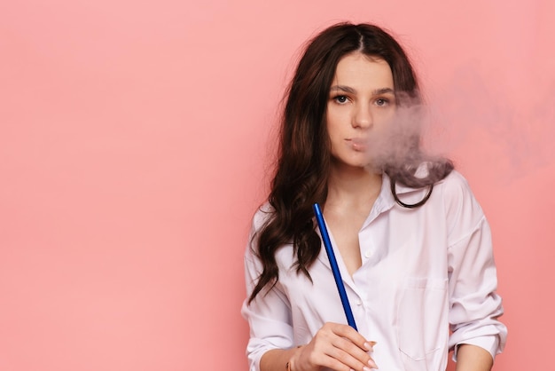 Mujer joven fuma una cachimba sheesha sobre un fondo rosa El placer de fumar