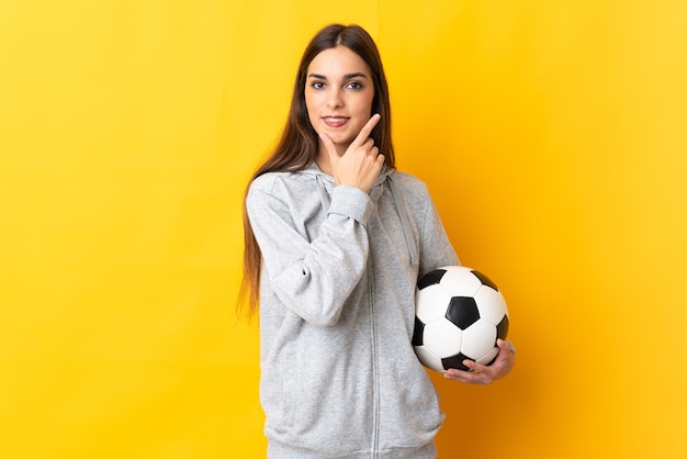 Mujer joven futbolista aislada en amarillo feliz y sonriente