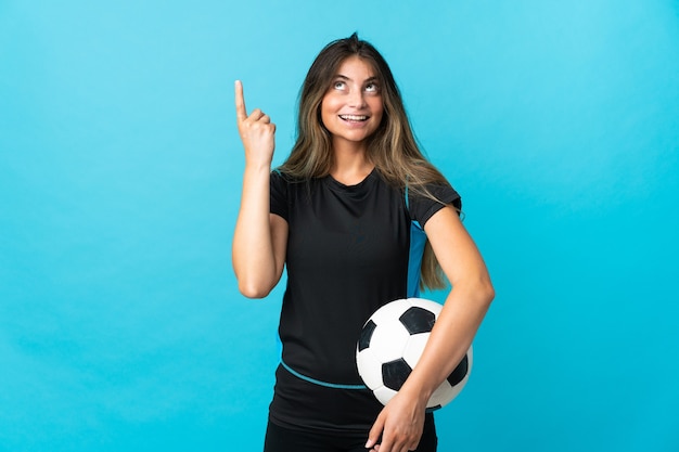 Mujer joven futbolista aislada en azul apuntando hacia una gran idea