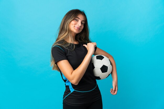 Foto mujer joven futbolista aislada en azul orgulloso y satisfecho de sí mismo