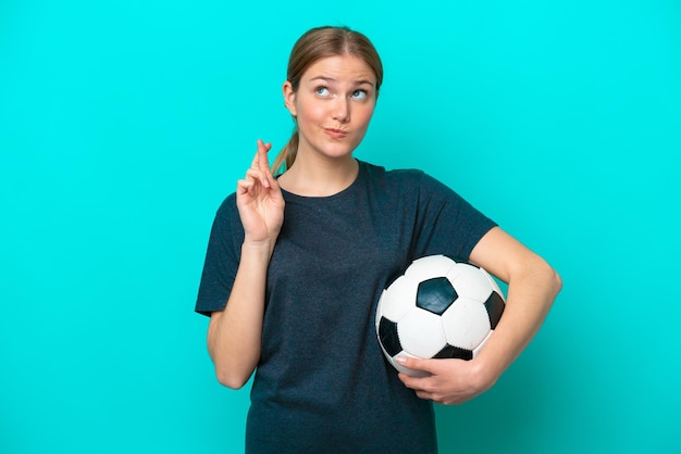 Mujer joven futbolista aislada de fondo azul con los dedos cruzados y deseando lo mejor