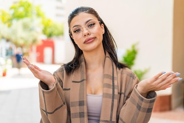 Foto mujer joven con gafas al aire libre haciendo gesto de dudas