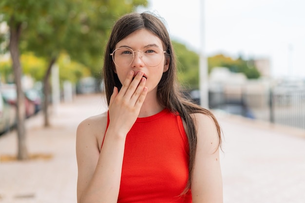 Mujer joven con gafas al aire libre sorprendida y conmocionada mientras mira hacia la derecha