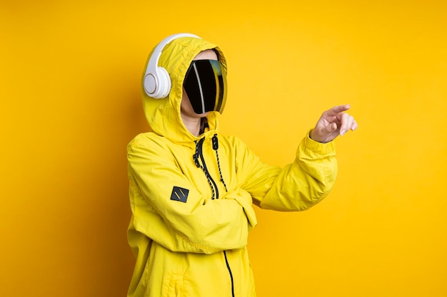 Mujer joven con gafas cyberpunk con auriculares hace clic en una pantalla virtual sobre un fondo amarillo