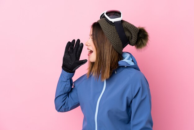 Mujer joven con gafas de esquí sobre pared rosa