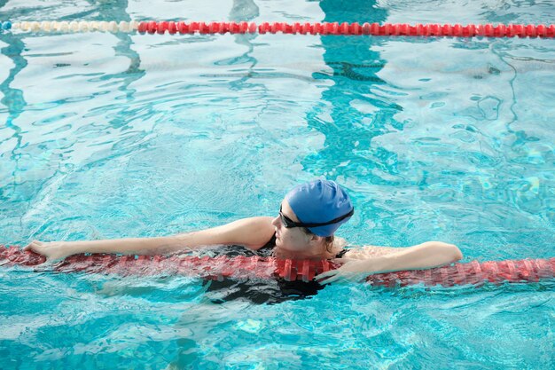 Mujer joven en gafas y gorra con divisor de carril mientras cruza la piscina