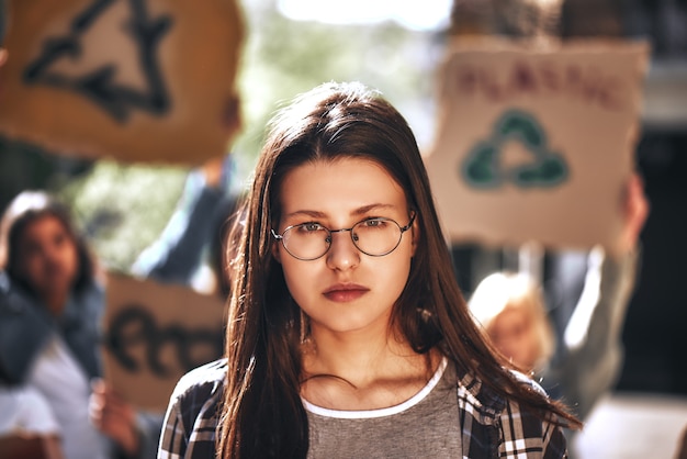 Mujer joven en gafas con un grupo de manifestantes sosteniendo letreros