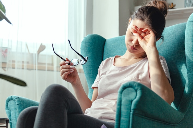 Mujer joven con gafas en las manos se sienta en una silla y sufre fr