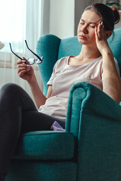 Mujer joven con gafas en las manos se sienta en una silla y sufre fr