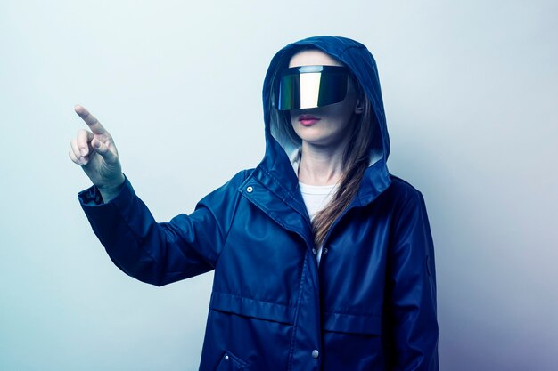 Mujer joven en gafas de realidad virtual presionando un dedo en una pantalla táctil sobre un fondo claro.