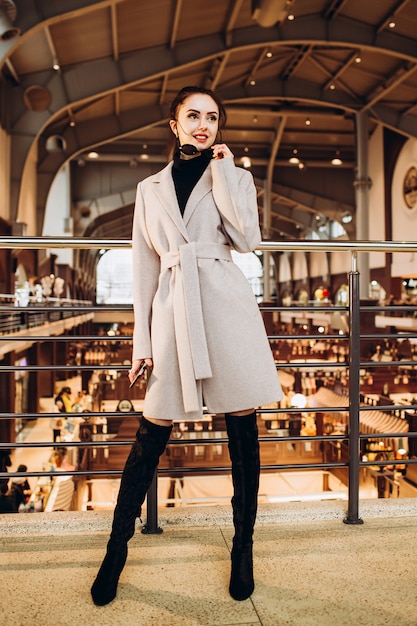 Mujer joven con gafas de sol, botas largas y abrigo gris