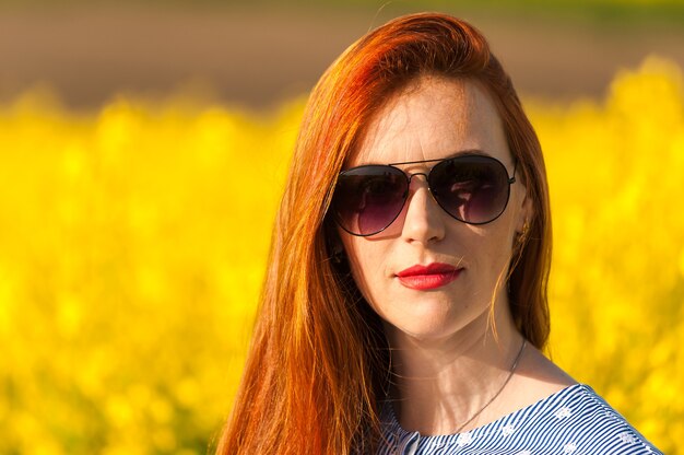 Mujer joven con gafas de sol en campo amarillo