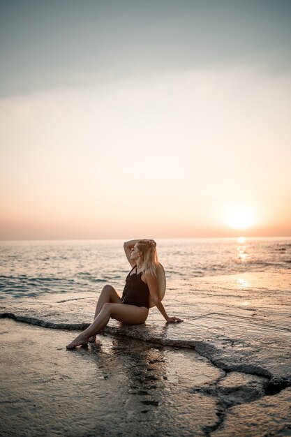 Mujer joven con gafas de sol descansa en el mar esbelta en traje de baño negro. Enfoque selectivo