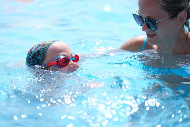 Mujer joven con gafas de sol enseñando a los niños a nadar en la piscina